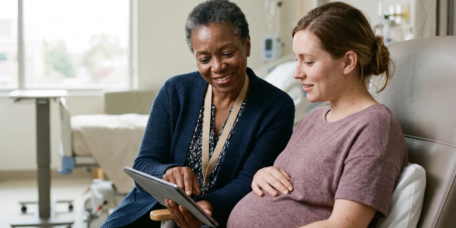 Hospital social workers can arrange postpartum housing before discharge A hospital social worker sitting beside a pregnant woman in a maternity ward, looking at a tablet together