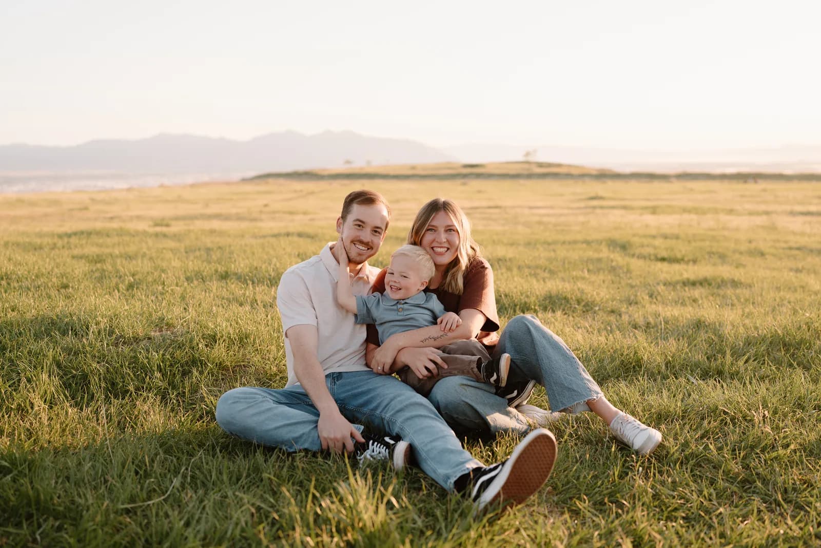 Andrew, Hailey, and Grayson sitting together in a golden sunlit field