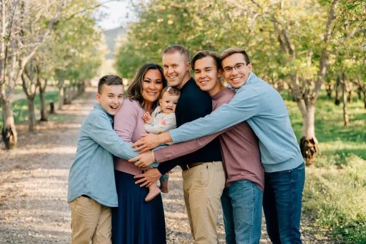 Nathan, Jessica, their three sons, and baby Betty hugging in an autumn orchard